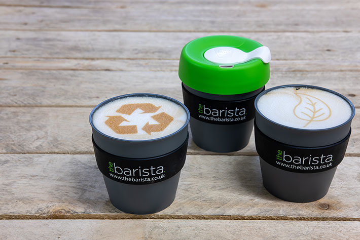 Reusable coffee cups with recycling icons in coffee foam